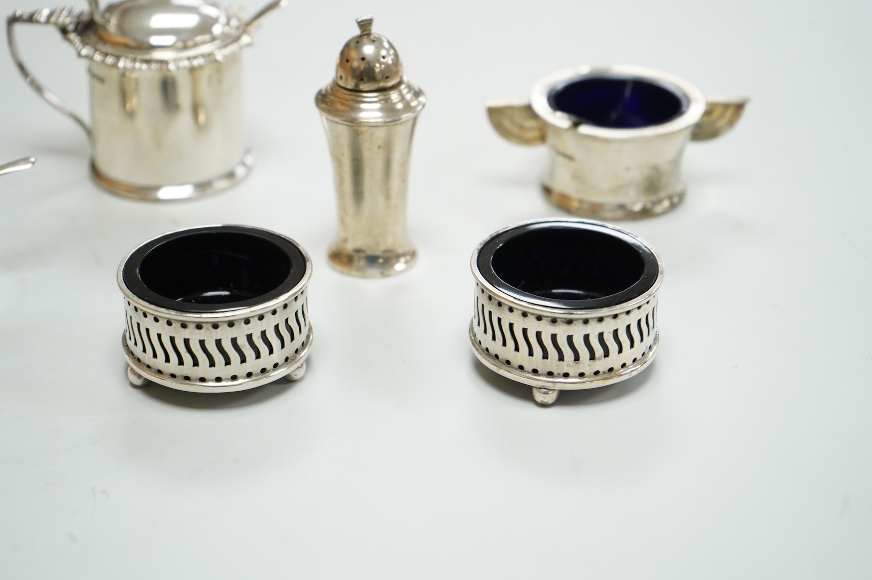 A George V Art Deco three piece silver condiment set and two spoons by William Adams Ltd, Birmingham, 1935, together with a pair of late Victorian pierced silver salts with blue glass liners and an Edwardian silver musta